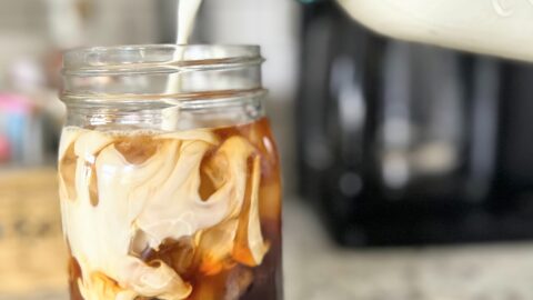 pouring-cream-into-iced-coffee-in-a-mason-jar-on-kitchen-counter