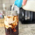 pouring-cream-into-iced-coffee-in-a-mason-jar-on-kitchen-counter