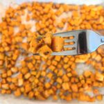 oven-roasted-sweet-potatoes-on-a-fork-in-front-of-a-baking-sheet-of-oven-roasted-sweet-potatoes
