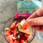 person holding chip with pico de gallo and bowl underneath
